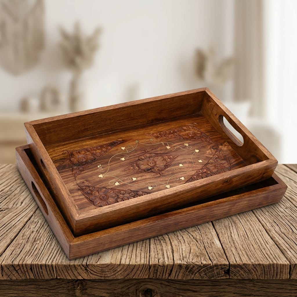 Two rectangular wooden serving trays with cutout handles, stacked on a rustic wooden table. The top tray features an inlaid floral and geometric pattern in darker and lighter wood tones with small gold-colored accents.